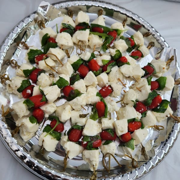 Silver platter of skewered mozzarella, cherry tomatoes, and fresh basil arranged as caprese appetizers.