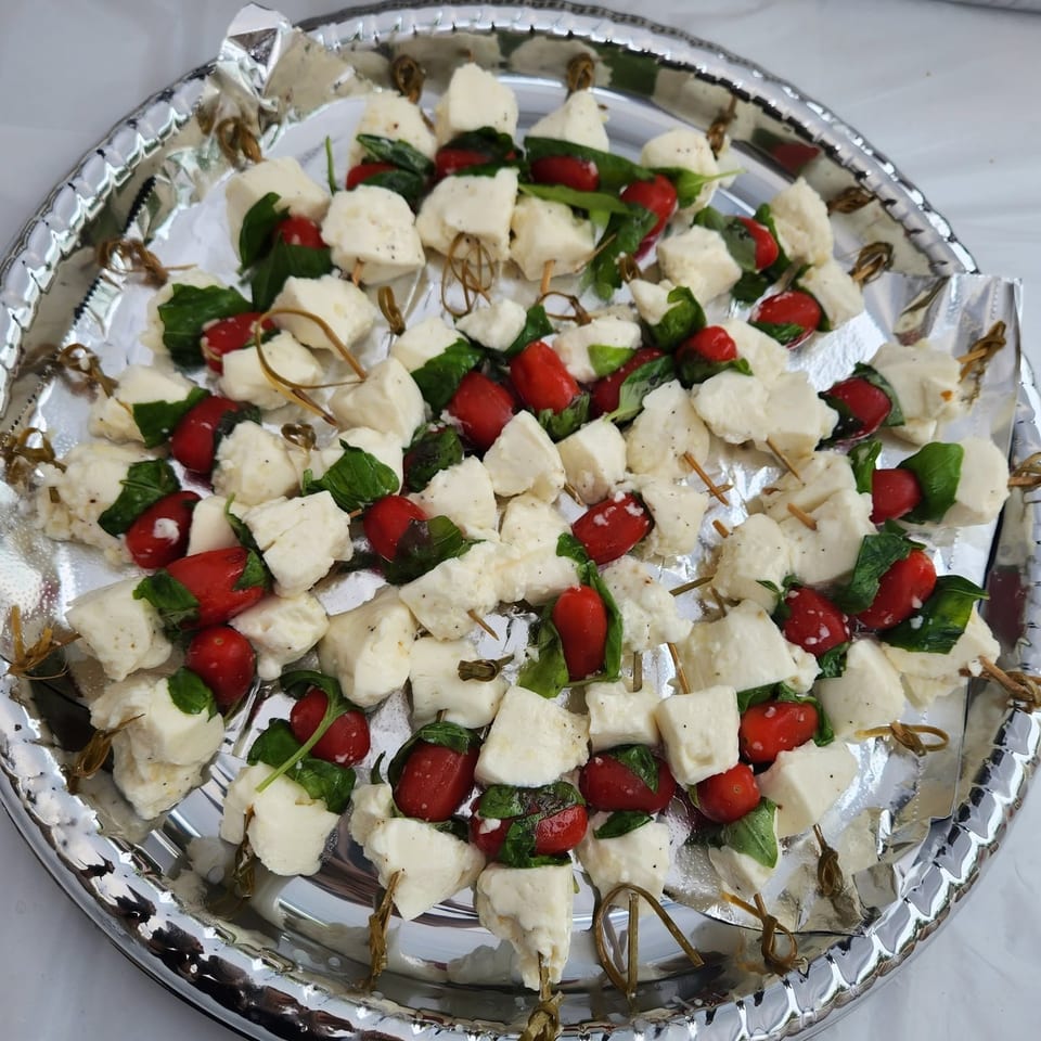 Silver platter of skewered mozzarella, cherry tomatoes, and fresh basil arranged as caprese appetizers.