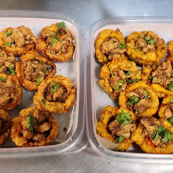 Two containers hold golden fried shrimp fritters topped with seasoned shrimp and fresh cilantro.