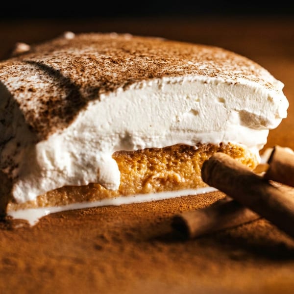 Cinnamon-dusted tiramisu slice with creamy layers and cinnamon sticks on a warmly lit wooden table.