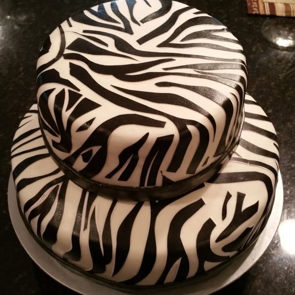 Two-tier round cake decorated with bold black-and-white zebra stripes on a white cake board atop a dark countertop.