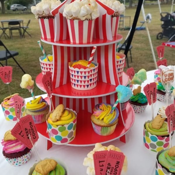 Colorful carnival-themed dessert display with cupcakes, popcorn, cotton candy, and marshmallow-topped treats at an outdoor fair.