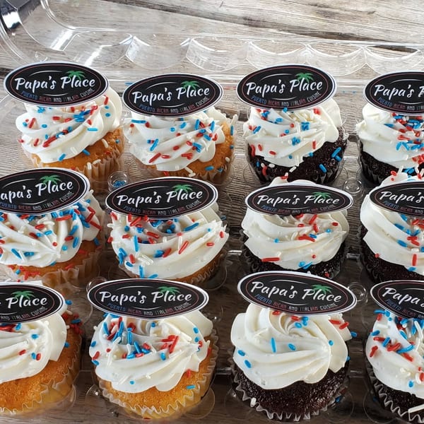 Twelve frosted cupcakes with red, white, and blue sprinkles, topped with Papa’s Place Puerto Rican and Italian Cuisine labels.