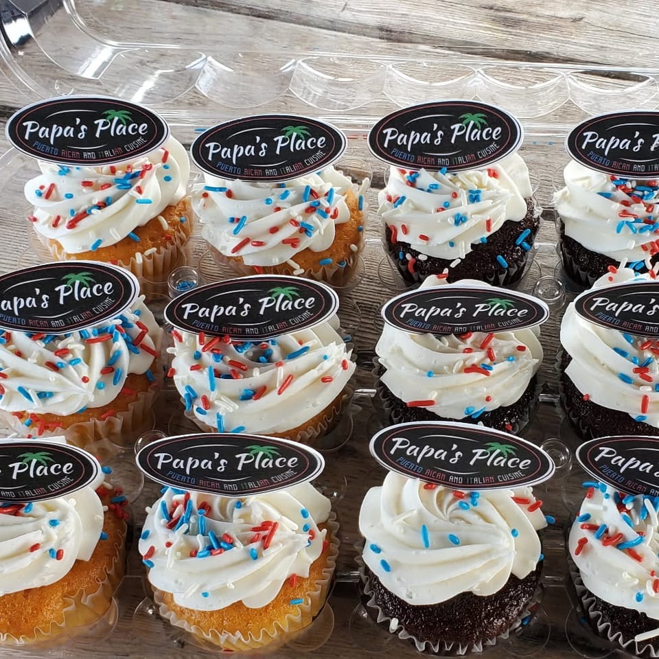 Twelve frosted cupcakes with red, white, and blue sprinkles, topped with Papa’s Place Puerto Rican and Italian Cuisine labels.
