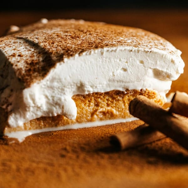 Creamy cinnamon-dusted dessert with a golden crust, accompanied by rolled cinnamon sticks on a warmly lit wooden surface.