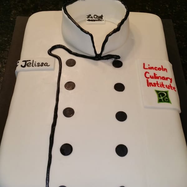 White rectangular cake decorated as a chef’s coat, featuring black buttons, piping, a chef logo, and Lincoln Culinary Institute lettering.