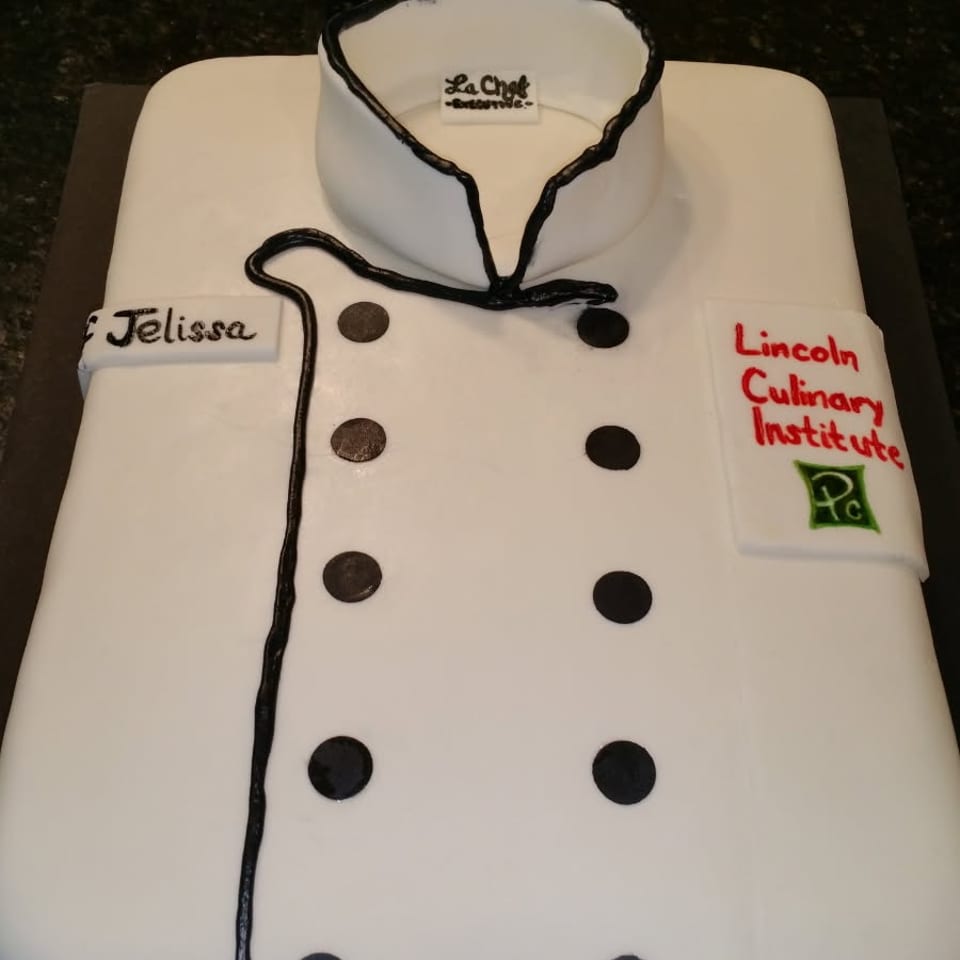 White rectangular cake decorated as a chef’s coat, featuring black buttons, piping, a chef logo, and Lincoln Culinary Institute lettering.