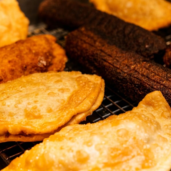 Assorted golden-brown pastries and dark grilled kebabs arranged on a cooling rack.