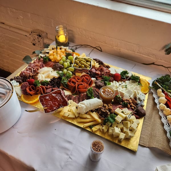 Abundant charcuterie and cheese platter arranged with meats, cheeses, grapes, olives, fruit, nuts, dips, and candlelit ambiance.