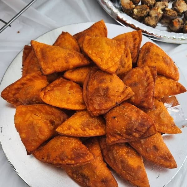 A plate piled with golden-brown triangular fried pastries sits beside a tray of browned stuffed mushrooms.