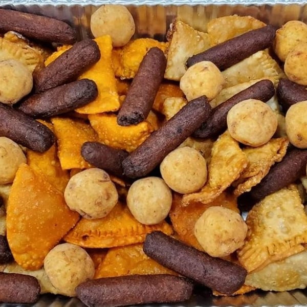 Aluminum tray filled with assorted golden fried pastries, round fritters, and dark cylindrical croquettes.