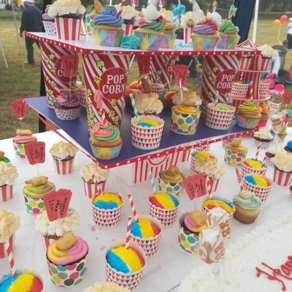Colorful popcorn-themed cupcakes and dessert cups arranged on a tiered display at an outdoor fair.