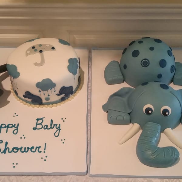 Two decorated baby shower cakes featuring a smiling elephant and a spotted round cake, with teal and brown accents.