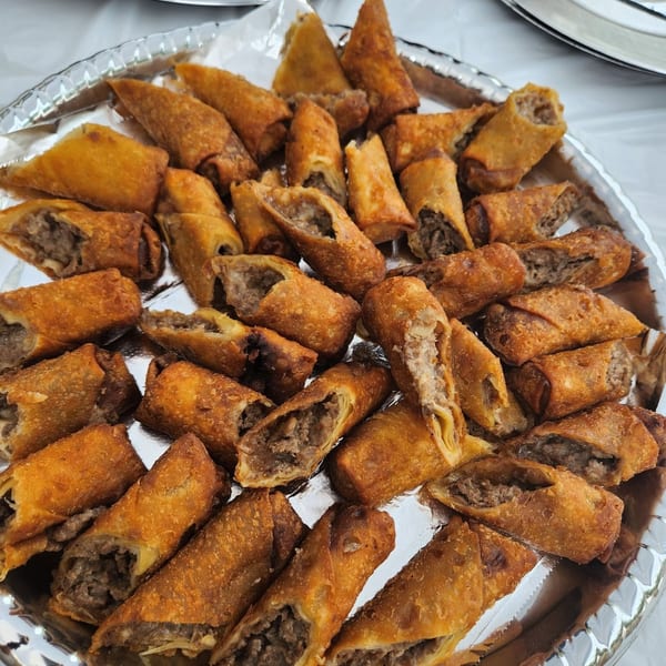 Large platter of golden fried meat-filled pastries, with additional stuffed mushrooms and pastries on surrounding trays.