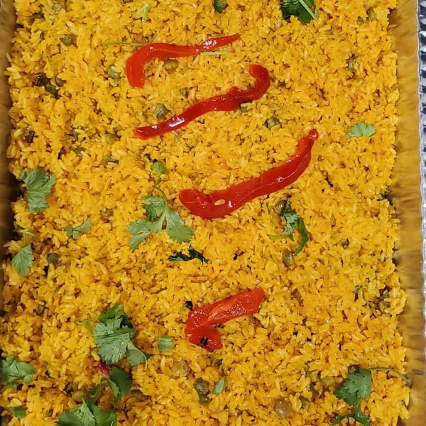 Tray of golden spiced rice with peas, cilantro, and red pepper strips.