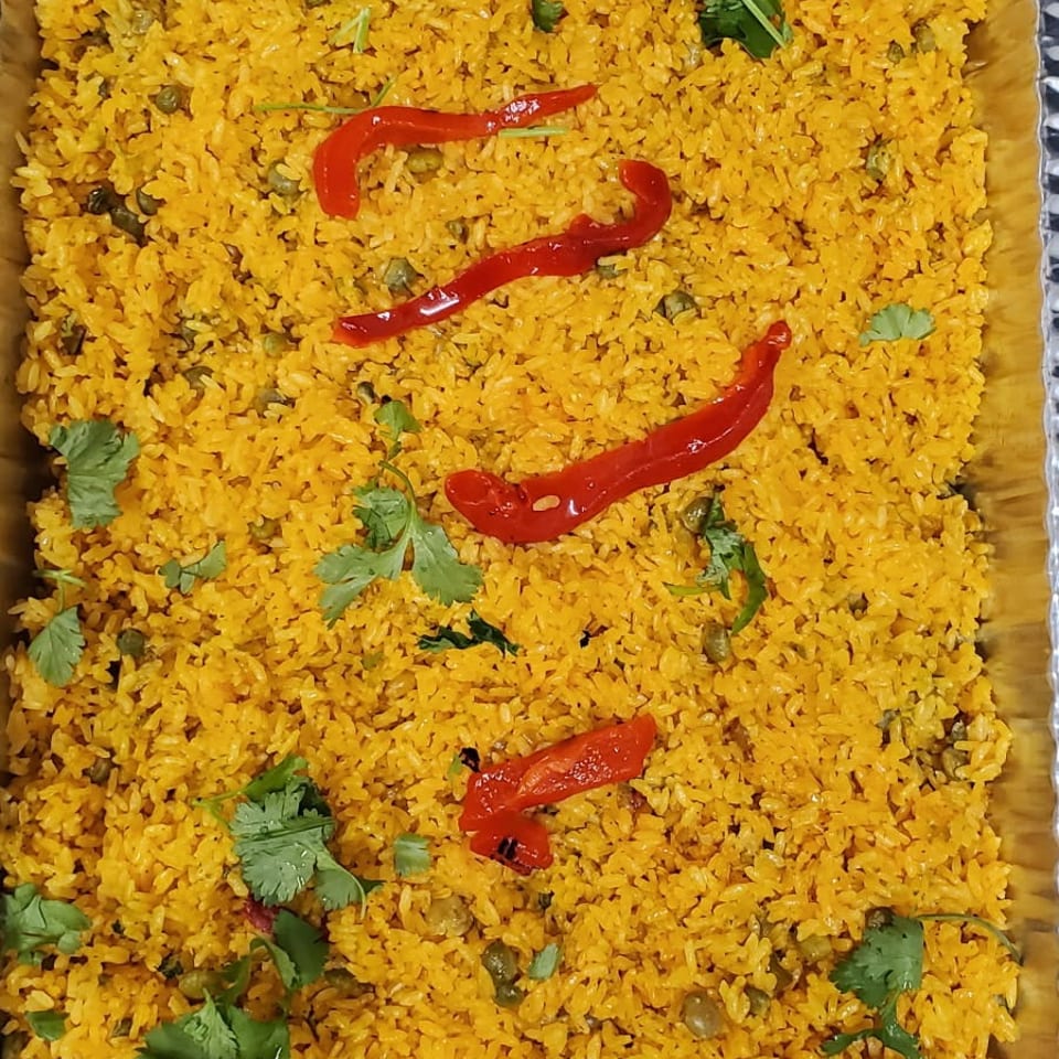 Tray of golden spiced rice with peas, cilantro, and red pepper strips.
